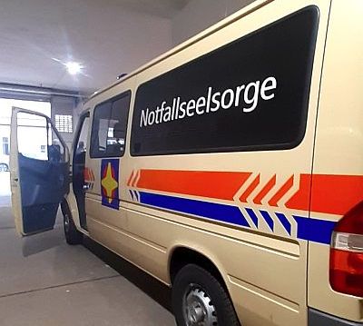 Ein Einsatzfahrzeug in der Größe eines Kleinbusses steht mit offener Fahrertür in der Garage bereit. Es sieht einem Krankenwagen ähnlich und trägt den auffälligen Schriftzug "Notfallseelsorge".