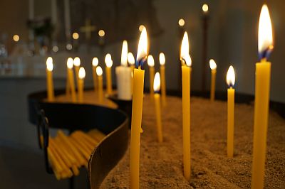 Gelbe Kerzen stehen aufeinem Halter in einem abgedunkelten Raum und geben ihm einen warmen Schein.