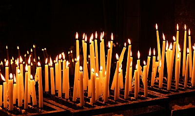 Auf einem Gestell in einem weiten dunklen Raum stehen viele brennende Kerzen. Kurze, lange, gerade oder schief, alle sind schlank und aus dem gleichen gelben Wachs, so gleich und doch so verschieden. Die Kerzen stehen und leuchten so, wie vorbeikommende Menschen sie als ihr Zeichen für eine Hoffnung oder eine Bitte gestiftet haben.