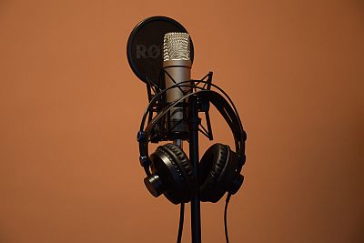 Auf einem Stativ steht ein Studiomikrofon mit Knallschutz, davor hängt ein Kopfhörer. Es herrscht offensichtlich Ruhe.