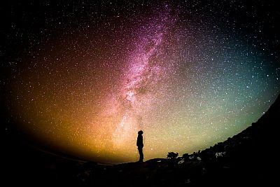 Ein sehr heller Sternenhimmel mit der Milchstraße prangt, fotografisch zu einer Kugel verzerrt, über dem Schatten eines Menschen, der staunend nach oben schaut.
