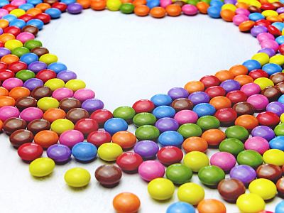 Auf einem Tisch sind viel bunte Smarties (dragierte Schokoladenplätzchen) ausgebreitet. In der Mitte ist eine Lücke in Form eines Herzens.