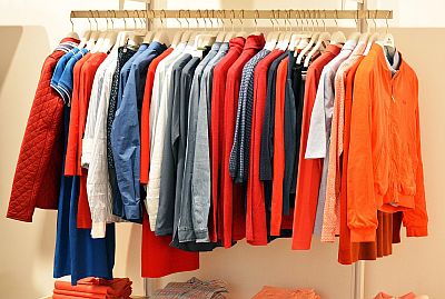 Auf einem industriellen Garderobenständer hängt auf Bügeln viel bunte Kleidung zum Anprobieren, vielleicht zum Verkauf.