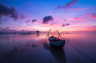 Ein Fischerboot schwimmt unbemannt auf einem See. Es ist noch fast dunkel und recht kühl. Aber am Horizont kündigt sich der Sonnenaufgang an.