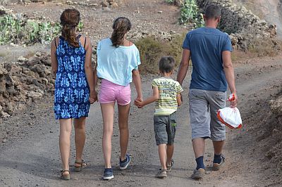 Wir sehen auf eine Familie, die mit leichtem Gepäck in sommerlicher Kleidung vor uns her wandert.