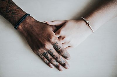 Zwei Hände, die einer farbigen und einer weißen Frau, liegen ineinander. Beide haben Freundschaftsarmbänder.
