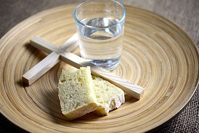Auf einem Teller liegen zwei Stücke Brot und ein Kreuz und steht ein Glas Wasser.