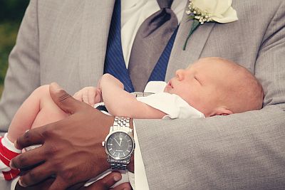 Ein Säugling liegt schlafend im Arm eines festlich gekleideten Mannes.