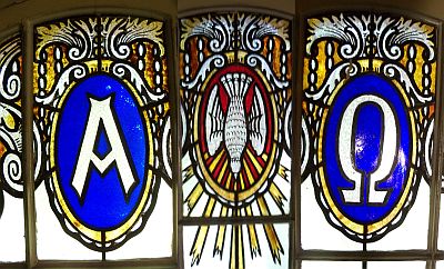 Wir sehen drei Ausschnitte aus Fenstern der Apsis der Woltersdorfer Kirche nebeneinander. Links ein A wie Alpha, in der Mitte die im Sturzflug vom Himmel herabfahrende Taube als Symbol des heiligen Geistes und rechts das Omega als letzter Buchstabe des Alphabets.