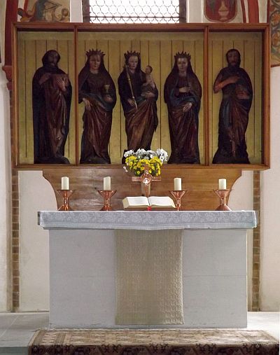 Foto: Altar mit Steinsockel und -tisch sowie einem dreiflügligen Aufbau aus Kästen. in denen vor goldenem Hintergrund fünf geschnitzte Figuren stehen
