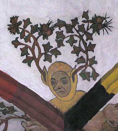 Ein Foto zeigt nahe des Schnittpunktes der Gewölberippen den Kopf eines Mannes in einem mittelalterlichen Narrenkostüm. Aus seinen spitzen Ohren ragen sich verzweigende Äste mit Blättern und stacheligen Blüten heraus und umgeben seinen Kopf.