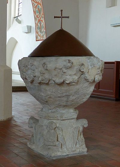 Foto: ein zirka 1 Meter hoher kelchförmiger Taufstein aus Stein. Auf seiner runden Öffnung sitzt eine kegelförmige bronzene Haube mit einem schlichten Kreuz.